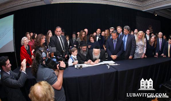Rabbi Aaron Slonim flanked by his grandson, Mendel Slonim (age seven), holds the quill as the first word is inscribed in the Binghamton Legacy Torah